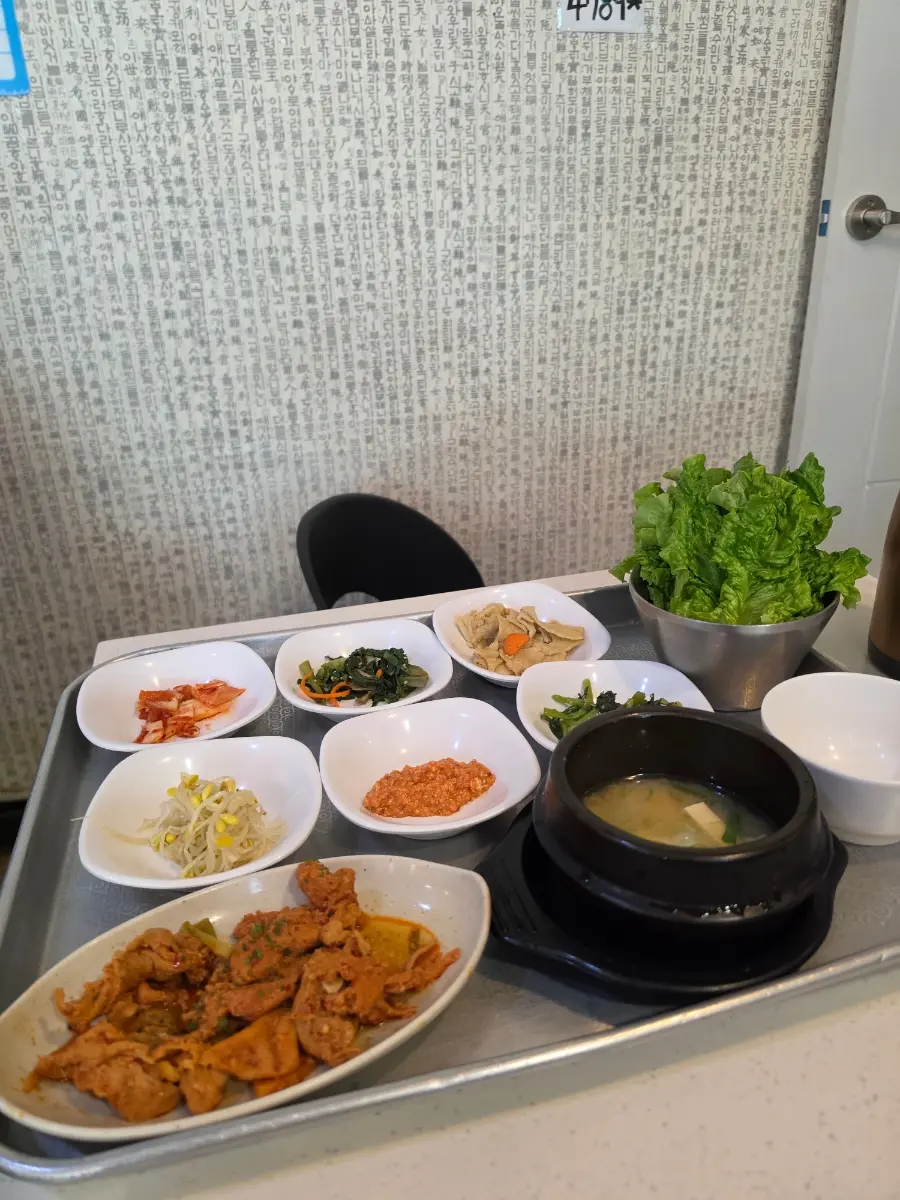 A complete Jeyuk Ssambap set meal with spicy pork, stone pot rice, and five side dishes